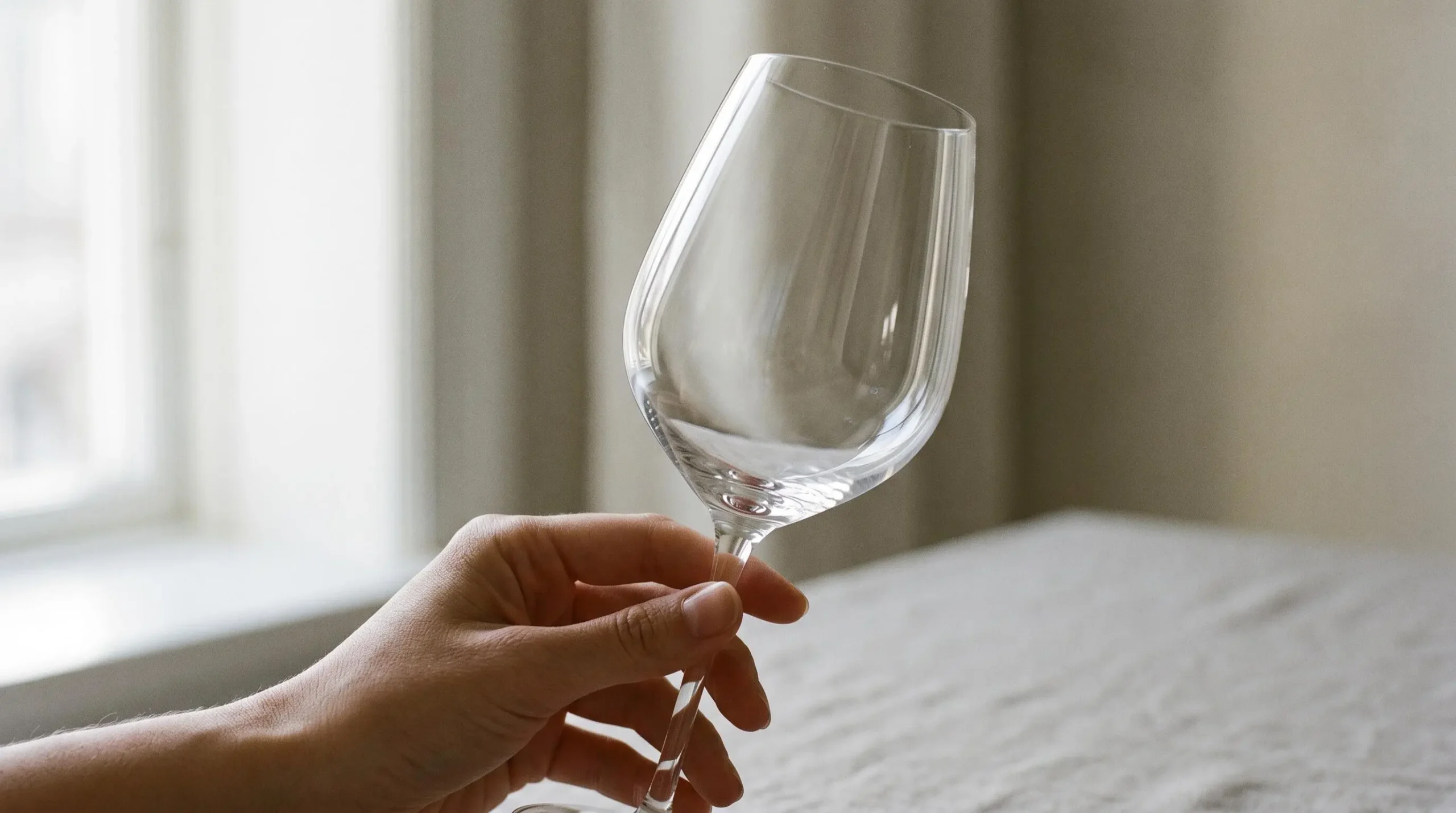 Gros plan main tenant délicatement verre tulipe cristallin vide, lumière naturelle traversant paroi fine révélant transparence matériau, arrière-plan flou beige